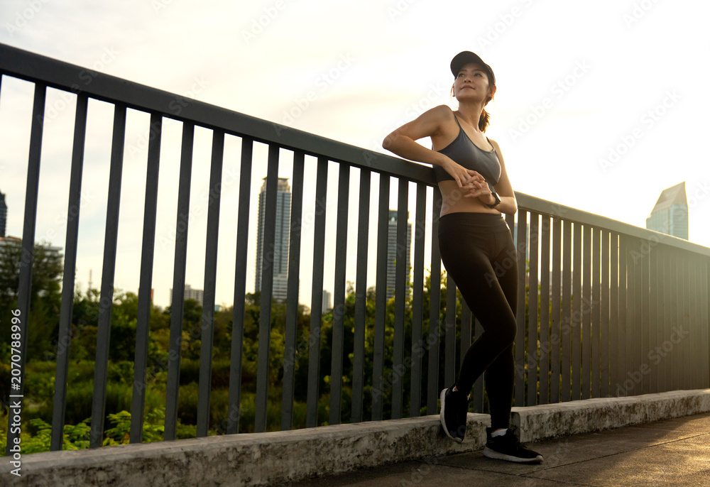 Naklejka premium Wide shot of Asian sport girl lean on rail and look to her right side with smiling with warm light of evening.