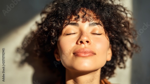 Woman with curly hair breathing deeply with eyes closed. Calm girl practicing mindfulness for emotional balance. Concept of menopause relief, stress management and mental wellness.