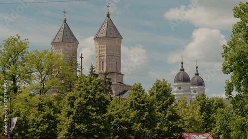The Monastery of the Holy Three Hierarchs stands tall among trees in Iasi. Sunlight shines on the buildings, creating a beautiful urban view that captures attention.