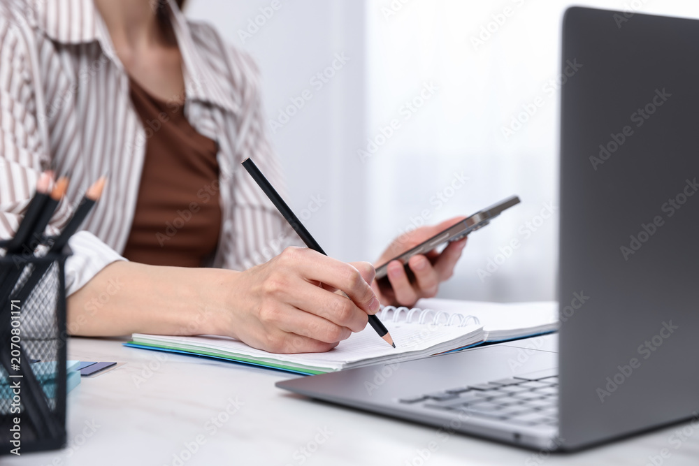 Fototapeta premium Young woman using laptop and smartphone at workplace in kitchen, closeup