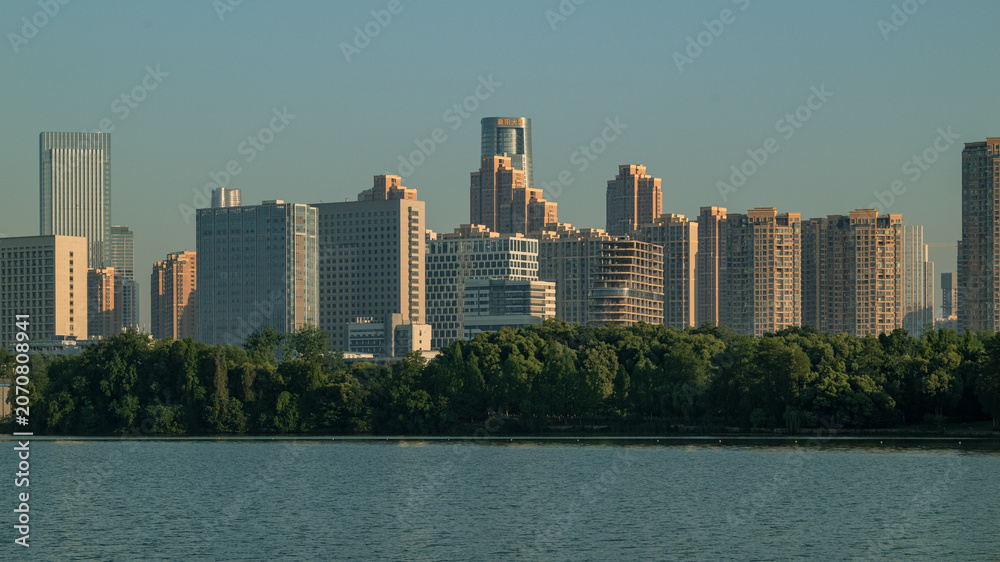 Fototapeta premium Modern city skyline across a waterfront with trees in evening light