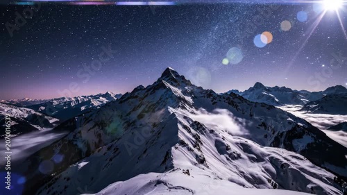 Snowy mountain peak under indigo starry sky with drifting clouds and sweeping lens flare