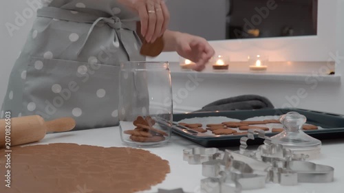 Woman places baked gingerbread cookies from tray into glass storage jar. Female chef packs biscuit dessert inside kitchen room for holiday pastry food preservation culinary lifestyle process.