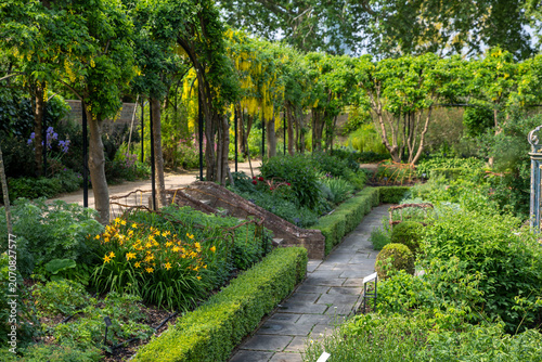 фотографія A picturesque stone path winding through the lush gardens of Kew with a beautiful yellow laburnum archway and colorful flowerbeds
