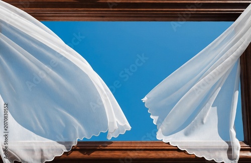 Sheer White Curtains Billowing In Breeze Against Clear Blue Sky Through Wooden Window Frame For Freedom And Openness Concepts