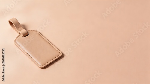 A light brown leather luggage tag with clear stitching lies flat on a smooth peach surface