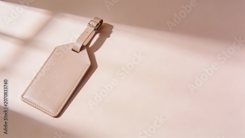 A single light brown leather luggage tag with a metal buckle strap rests on a smooth, light pink background