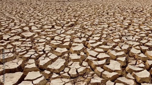 A wide shot of barren, cracked earth under a stark sky. The parched ground stretches endlessly, showcasing the devastating effects of drought