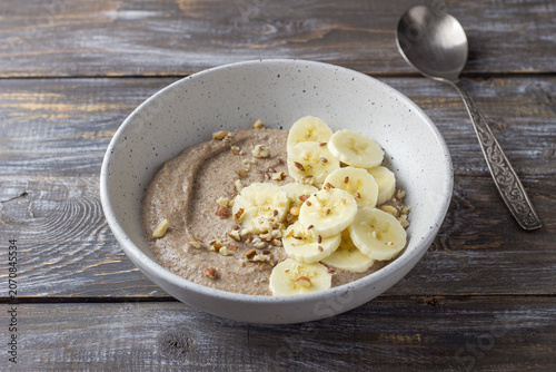 Healthy flaxseed porridge topped with banana slices, chopped nuts and seeds in a ceramic bowl. Nutritious breakfast with natural ingredients, copy space