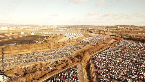 Aerial view of a vast new car storage facility filled with thousands of parked vehicles, situated near a highway bridge in Gloucestershire, United Kingdom.