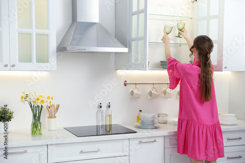 Bild auf Leinwand Woman putting clean glasses into cabinet in kitchen, back view