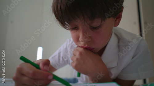 Fényképezés Young boy concentrating while drawing with colored pencil and resting chin on ha