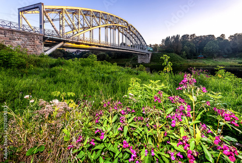 View on the arch bridge across the Msta river in summer day in sunset light. Built in 1905. Borovichi, Russia