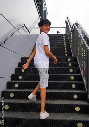 street style. Teenage boy, wearing a cool and casual summer outfit, happily climbs some metal stairs. copy space