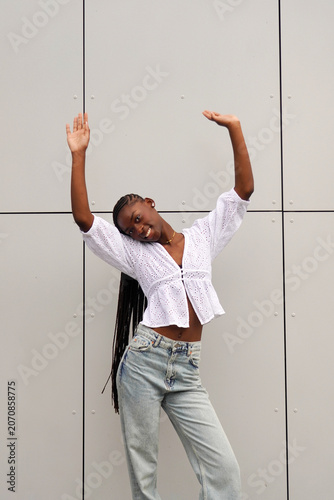 street style. beautiful smiling afro woman with braids hairstyle dancing in the street with her arms raised