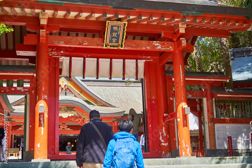 Quadro su tela Visitors walk toward a traditional bright vermilion wooden gate at a Japanese Shinto shrine