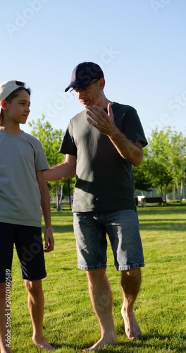 Father and son walking barefoot through park at sunset while talking and enjoying time together. Boy carries soccer ball as golden evening light highlights family connection and shared moments.