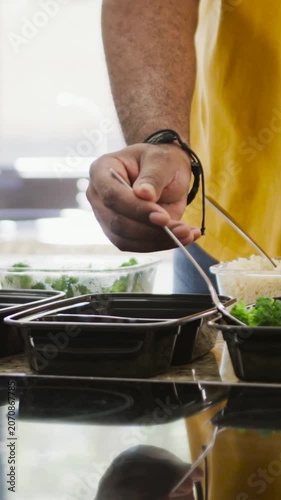 Vertical video: Yellow-sleeved hand filling bins of broccoli, rice at counter, copy space
