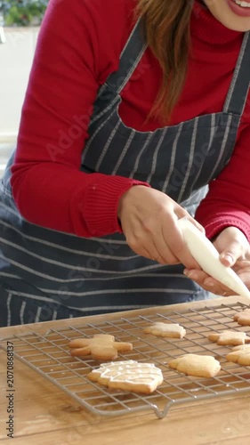 Vertical video: Picking up piping bag mom in apron piping icing on cookie rack for child in kitchen