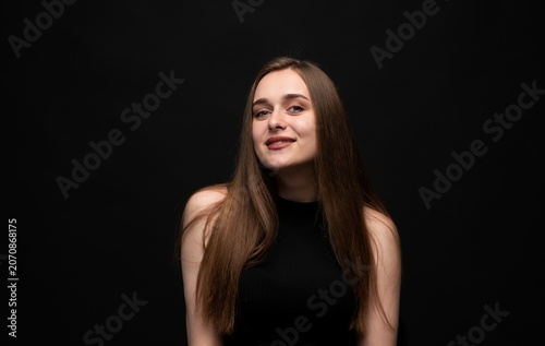 Young woman smiling confidently looking at camera, posing for studio portrait on black background, expressing beauty