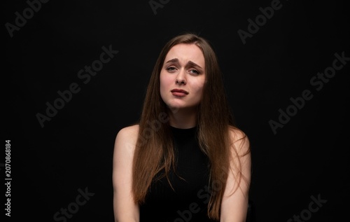 Young woman expressing fear, anxiety, and sadness against a dark background, reflecting stress, worry, and emotional distress