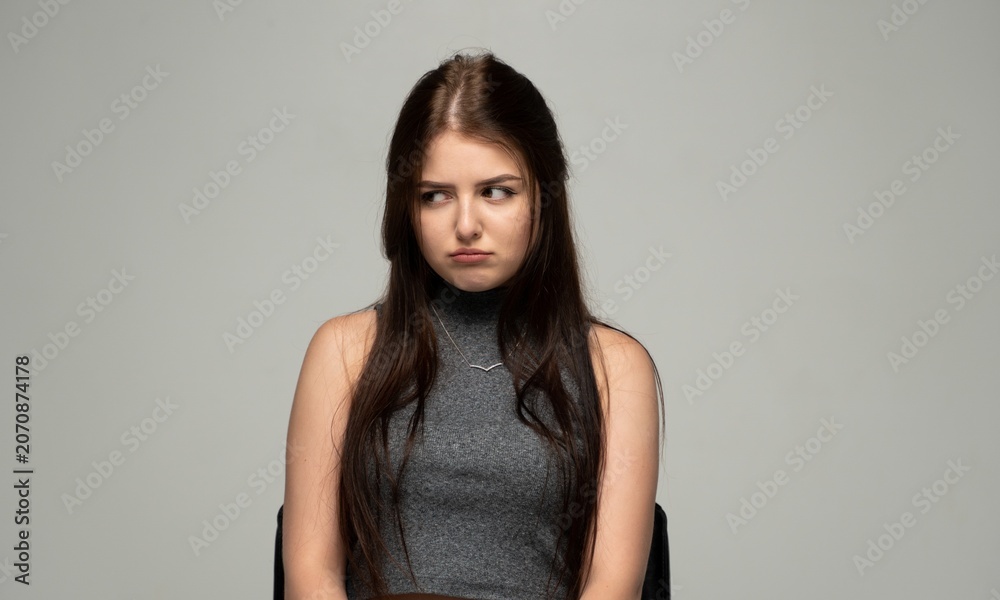 Naklejka premium Young woman expressing disinterest and disappointment, looking away with a sullen face and pouty lips