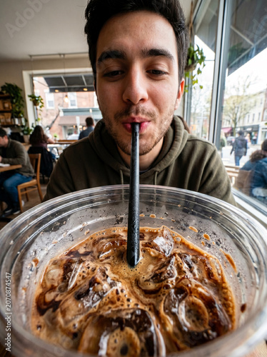 Young Man Enjoying Refreshing Iced Coffee with Straw in Casual Coffee Shop