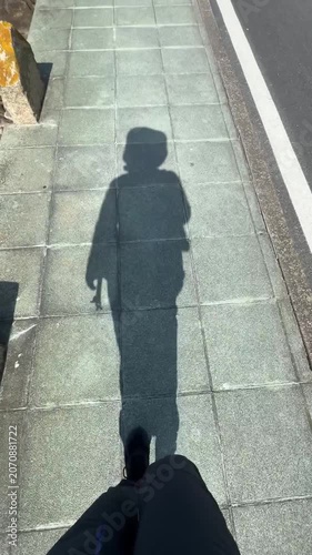 Pilgrim shadow moves along sunlit pavement on Portuguese Camino de Santiago route, walking motion, backpack silhouette. Pilgrimage journey, long distance hiking, solo travel, spiritual tourism