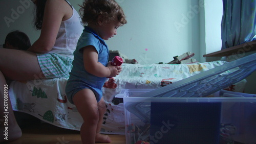 Tableau sur toile Curious toddler rummaging through toy storage box on bedroom floor while mother