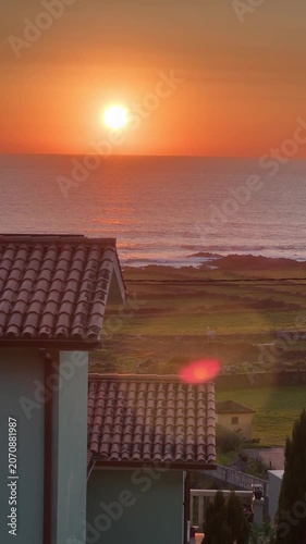 Sunset over Atlantic Ocean viewed from Oia, Pontevedra, Spain, with coastal village rooftops, shoreline, warm orange sky. Vacation atmosphere, seaside landscape, nature tourism
