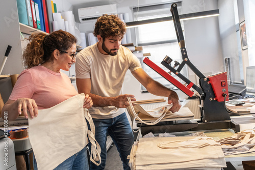 Konstfotografi A print shop worker is operating a heat press machine for textile printing, carefully aligning the material before pressing