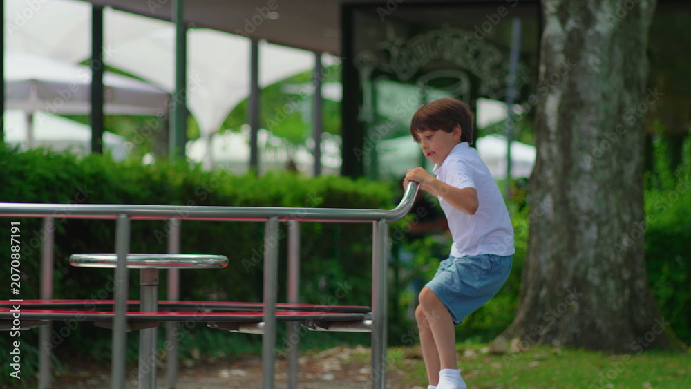 Fototapeta premium Young boy climbing onto playground carousel while preparing to spin ride, playful childhood moment expressing anticipation curiosity and outdoor activity