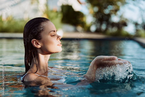 Schilderij op canvas Woman relaxes in a sunlit pool, eyes closed, calm expression, water ripples arou