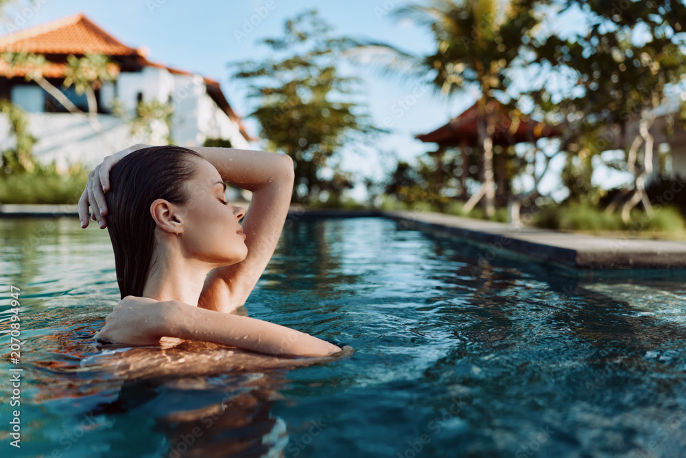 Fototapeta premium Woman in an outdoor pool with wet hair enjoying a tranquil moment. Sunlit blue water glitters, conveying lifestyle, wellness, and self care in a bright resort setting.