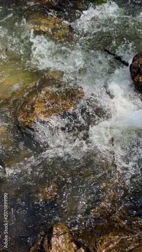 Fast flowing river stream rushing around mossy rocks with white foam and fallen leaves on bank