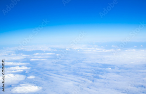 Beautiful aerial view of a vast cloud layer seen from an airplane at cruising altitude. Blue sky above and soft white clouds below create a peaceful travel and aviation background.