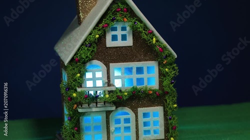 On a dark blue background and green covering, a decorated house with color-changing light in the windows