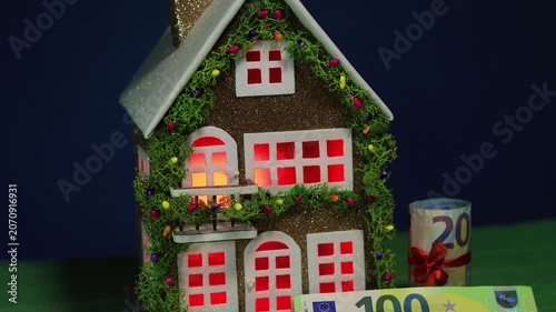 On a dark blue background and green cover there is a decorated house with euro banknotes nearby
