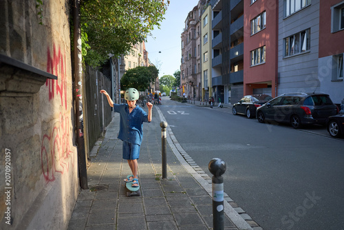 Young boy in helmet skateboarding down a city sidewalk on a sunny day