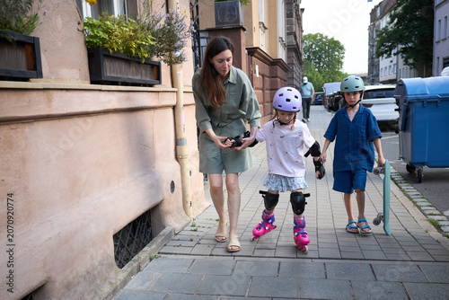 Mother teaching her children rollerblading and skateboarding on a city sidewalk