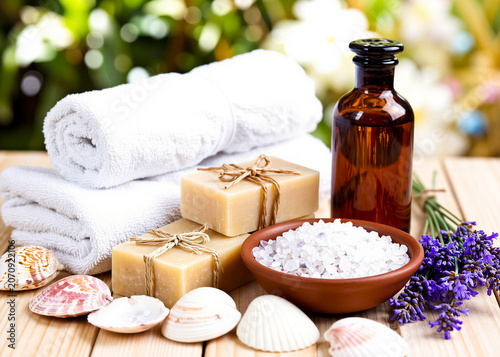 A tranquil spa arrangement featuring soft white towels, handmade soap, a bowl of sea salt, shells, lavender flowers, and an amber bottle