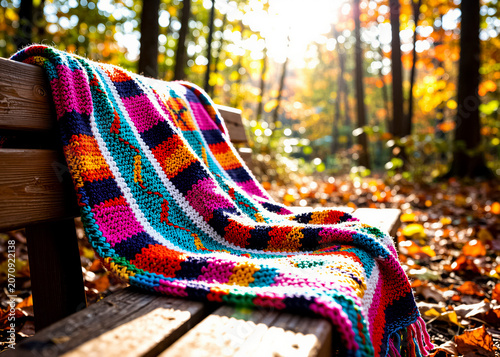 A colorful knitted blanket draped over a wooden bench in an autumn forest at dawn