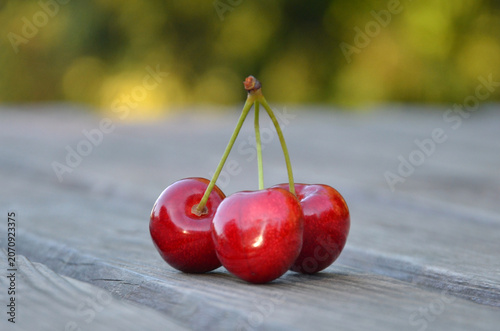 Three glossy red ripe cherry berries on wooden table background. Closeup, outdoors , isolated. Summer, cherry berry, fruits harvest.