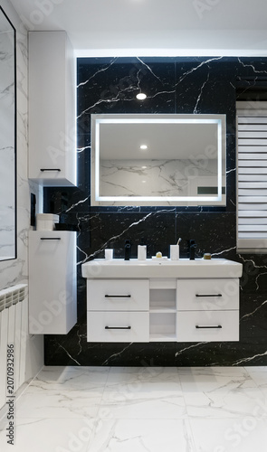 Modern bathroom with white wooden furniture led mirror and black marble stone on wall and white grey glaze floor