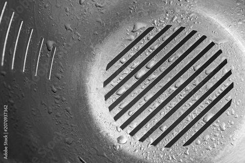 Close-up of a stainless steel colander covered with water droplets, featuring a geometric drainage pattern and reflective metallic surface.