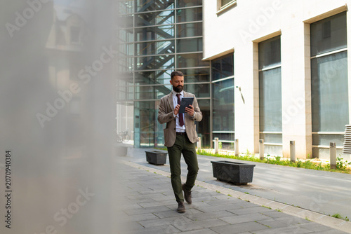 Bild auf Leinwand Businessman walking in city street using tablet