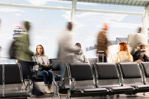 Obraz na plátně Passengers resting on airport waiting chairs next to blurry people rushing, long exposure movement, travelers in air transport hub standing in line at boarding gate next to seated tourists