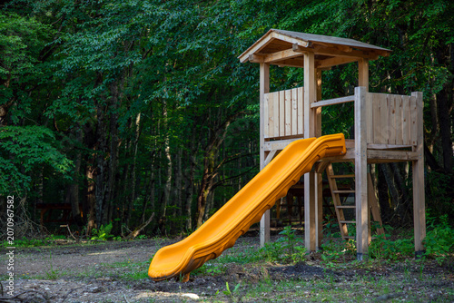 Wooden playground structure with a bright yellow slide inviting children to enjoy outdoor activities. Promoting playfulness. Leisure. Wellbeing