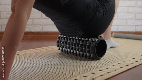 Woman massaging her thighs with a foam roller. Woman is massaging her thighs and glutes on a foam roller to relieve muscle tension and pain. Self-massage technique for myofascial release