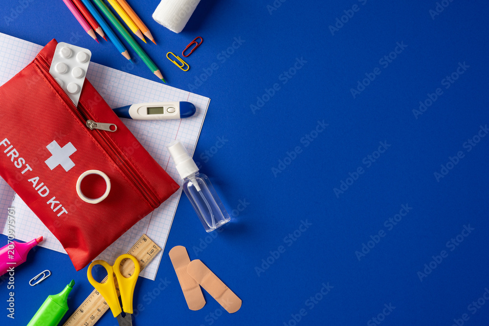 Fototapeta premium First aid kit and school supplies arranged on blue background for student health and safety preparedness